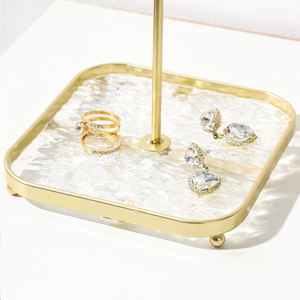 Textured glass tray base of the gold jewelry stand holding rings and earrings