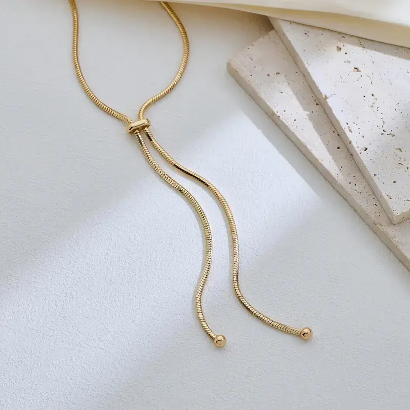 Gold-tone snake-chain lariat necklace flat lay showing slider and ball-tip ends